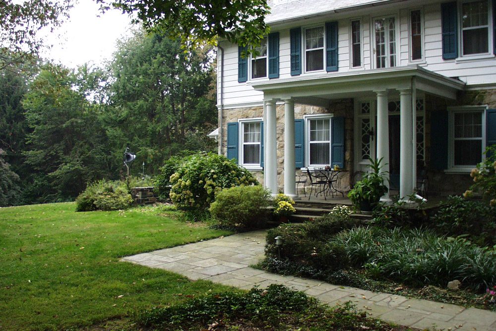 Stone home with layered foundation plantings and a bluestone walkway by Fine Garden Creations